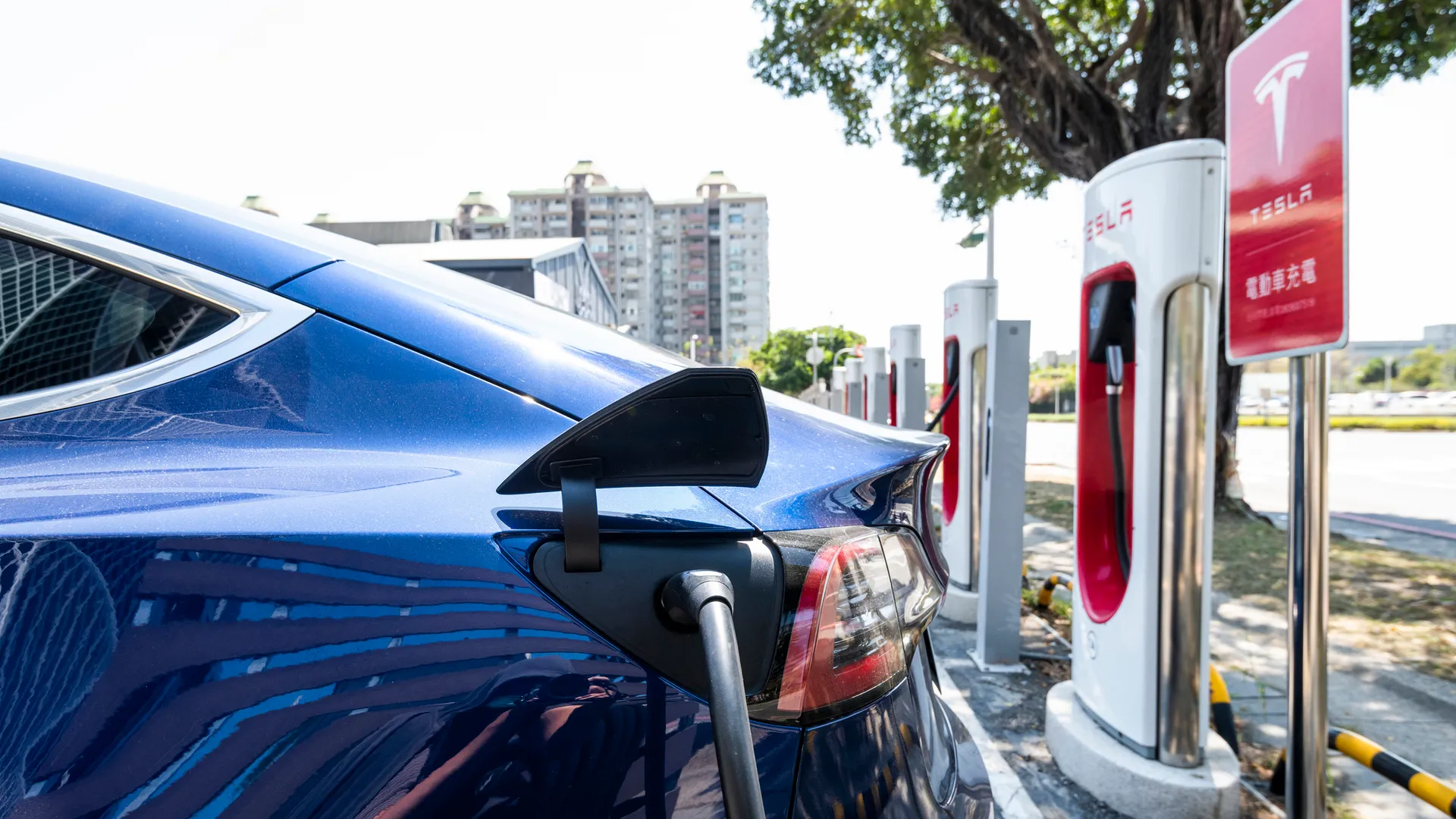 An electric car plugged in and charging at a row of public fast chargers